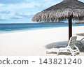 Thatched parasol umbrella and white lounge chairs on tropical sand beach facing calm turquoise ocean water under cloudy blue sky 143821240