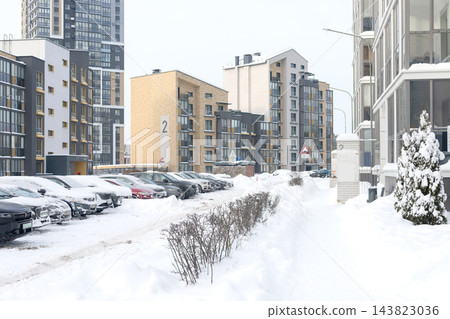 Residential courtyard with parked cars covered in winter snow near apartment buildings. Modern high rise condominium facade, snowdrift parking lot. Multistory architecture, balcony windows. Residential courtyard with parked cars covered in winter snow near apartment buildings. Modern high rise condominium facade, snowdrift parking lot. Multistory architecture, balcony windows. 143823036