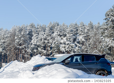 Dark suv parked near snowdrift, car in winter parking lot by snowy pine forest. Crossover vehicle on snow covered road near treeline, blue sky. Scandinavian woodland, frosty chilly day, Dark suv parked near snowdrift, car in winter parking lot by snowy pine forest. Crossover vehicle on snow covered road near treeline, blue sky. Scandinavian woodland, frosty chilly day, 143823105