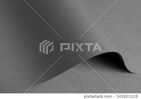 Woven gray paper texture, curled sheet with fold and curve. Folded designer paper close up, matte surface bent with gentle shadow. Minimalistic abstract backdrop, neutral material. 143823128
