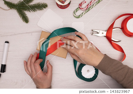 A person wraps a Christmas gift in a kraft box with green ribbon on a craft workspace A person wraps a Christmas gift in a kraft box with green ribbon on a craft workspace 143823967