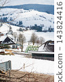 Snow-covered village landscape with rolling hills and farmhouses in winter, showcasing tranquility and natural beauty amidst the seasonal chill 143824416