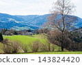 Vibrant spring landscape showcasing a quaint church amidst rolling hills and bare trees under a clear blue sky in the peaceful countryside 143824420