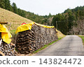A neatly stacked pile of firewood rests alongside a tranquil rural road, surrounded by a serene forest landscape on a cool autumn day 143824472