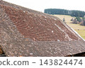 Roof shingles weathered by time overlook a serene hillside, capturing the charm of rural architecture in a tranquil landscape 143824474