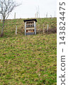 Hilltop structure overlooks lush green hillside under a cloudy sky during a serene afternoon, showcasing simple architecture in harmony with nature's beauty 143824475