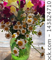 A beautiful bouquet of small white chamomile flowers with golden yellow centers arranged in a translucent green glass vase on a wooden table. Close-up floral photography, rustic home decor  143824710