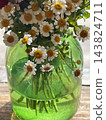 A beautiful bouquet of small white chamomile flowers with golden yellow centers arranged in a translucent green glass vase on a wooden table. Close-up floral photography, rustic home decor  143824711