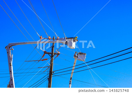 Workers in bucket truck service overhead power lines on location is not identified. 143825748