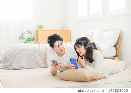 夫婦在床上看智慧型手機 143825990