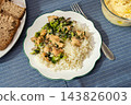 Rice with chicken breast, broccoli, and sesame seeds is served on a plate with hummus and bread on a table during breakfast at home 143826003