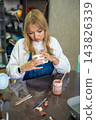 Young woman smoothing glaze on handmade ceramic mug with finger after painting. Removing air bubbles and imperfections represents finishing process in pottery craft 143826339