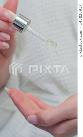 Woman in bathrobe applying hyaluronic collagen vital drops on hands. Skincare routine after morning showering. Woman in bathrobe applying hyaluronic collagen vital drops on hands. Skincare routine after morning showering. 143826917