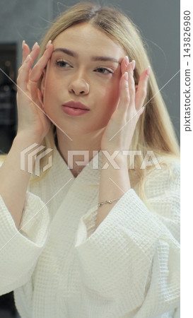 Attractive woman touching face after applying cream do make up looking in mirror. Skin care treatment. Healthy skin care treatment concept. 143826980