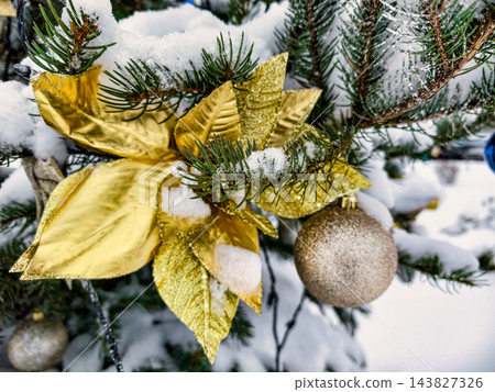 A Christmas and New Year tree is covered in snow. The tree features gold leaves and ornaments. This scene captures a winter celebration atmosphere A Christmas and New Year tree is covered in snow. The tree features gold leaves and ornaments. This scene captures a winter celebration atmosphere 143827326