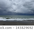 Stormy ocean waves breaking along dark sandy beach beneath dramatic layered clouds and gray horizon 143829692
