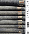Stacked denim jeans with visible waist and length size labels in shades of blue and gray fabric 143829693