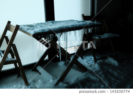 Wooden table and chairs covered in ice and snow near a bright window Wooden table and chairs covered in ice and snow near a bright window 143830774