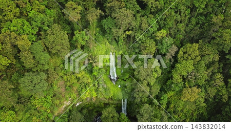 Sendang Gile waterfall plunges down a rocky cliff surrounded by lush green tropical rainforest, an untouched natural beauty and vibrant ecosystem of Lombok, Indonesia. Aerial view zoom in panorama 143832014