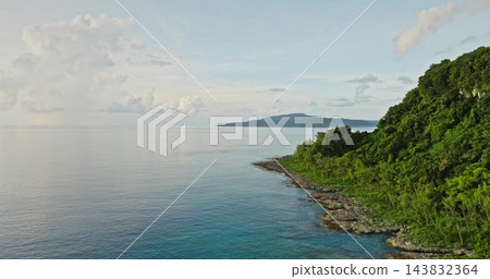 Tegua island landscape, part of the Torres islands in Vanuatu, features a rugged coastline with lush green tropical forest meeting the calm turquoise ocean under soft blue sky. Aerial drone flight Tegua island landscape, part of the Torres islands in Vanuatu, features a rugged coastline with lush green tropical forest meeting the calm turquoise ocean under soft blue sky. Aerial drone flight 143832364