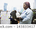 Businesswoman, laptop and typing as professional works while colleagues meet by strategy board. Productivity, digital workflow and coordination support flexible work on outdoor office terrace. 143833417