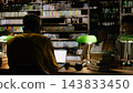 Adult learner, laptop and library frame rear view of man in yellow clothing working at computer near open books. Continuing education, research and digital skills shape study at communal table. 143833450