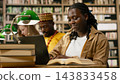 Student, laptop and book as smiling woman works on keyboard beside open reference text at library table. Digital learning, productivity and research connect academic reading with computer coursework. 143833458