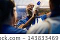 Soccer supporter, megaphone and raised arms center on man calling out to fans amid blue jerseys. Crowd coordination, fan leadership and team spirit energize chants in packed football stadium. 143833469