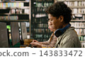 Student, focus and computer as young man looks down at workstation with headphones around neck and classmates behind. Independent learning, digital skills and concentration shape library study. 143833472