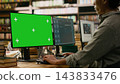 Green screen, monitor and computer mockup fill foreground while student types on keyboard in library. Screen replacement, digital learning and advertising offer editable desktop display context. 143833476