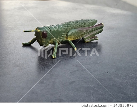 Decorative green grasshopper sculpture on gray surface 143833972
