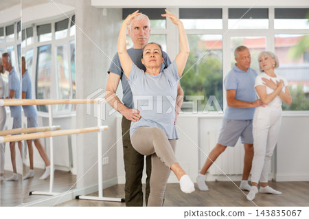 Positive duet of gymnasts rehearsing performance with support, mature modern ballet dancers in pair during group training session in ballet hall Positive duet of gymnasts rehearsing performance with support, mature modern ballet dancers in pair during group training session in ballet hall 143835067