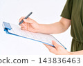 A woman's hands writing with a pen on a document on a clipboard. 143836463