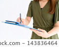 A woman writing on a clipboard while standing. 143836464