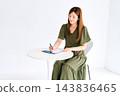 A woman filling out documents at a white table. 143836465