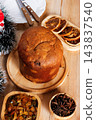 Whole Italian panettone on a bamboo tray, accompanied by candied fruits and dehydrated orange slices, set on a rustic wooden Christmas table 143837540