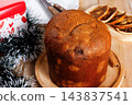 Whole Italian panettone on a bamboo tray, accompanied by candied fruits and dehydrated orange slices, set on an ornate, rustic wooden Christmas table 143837541