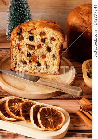 Sliced italian panettone, with a soft interior filled with raisins and candied fruit, arranged on bamboo boards atop a rustic wooden table. 143837544