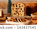Traditional Christmas panettone, sliced and filled with candied fruit, surrounded by dehydrated orange slices on a rustic wooden table 143837545