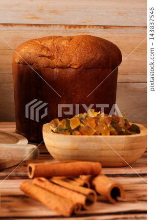 Whole Italian panettone on a bamboo tray, with candied fruits and dehydrated orange slices, on a rustic wooden table 143837546