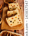 Slices of traditional Italian panettone filled with raisins and colorful candied fruits arranged on a bamboo board atop a rustic wooden Christmas table 143837547
