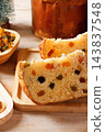 Slices of traditional Italian panettone, filled with raisins and colorful candied fruits, arranged on a decorated rustic wooden Christmas table 143837548