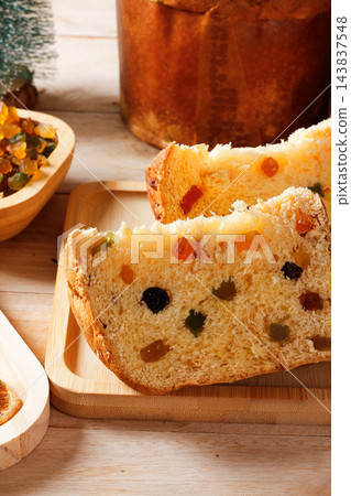 Slices of traditional Italian panettone, filled with raisins and colorful candied fruits, arranged on a decorated rustic wooden Christmas table 143837548