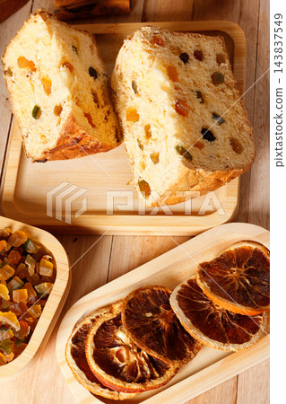 Slices of traditional Italian panettone, filled with raisins and colorful candied fruits, set on a rustic wooden Christmas table. 143837549