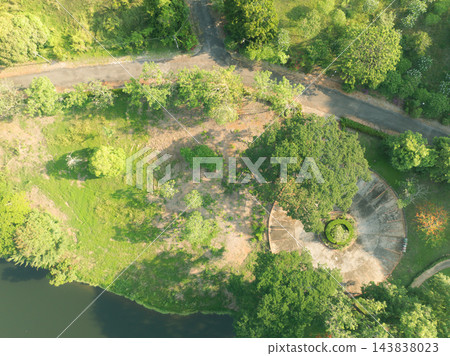 Top down aerial landscape of a tropical retreat resort garden with circular plaza, green lawn and lakeside trees in warm morning sunlight, offering a serene setting for relaxation and wellness travel. Top down aerial landscape of a tropical retreat resort garden with circular plaza, green lawn and lakeside trees in warm morning sunlight, offering a serene setting for relaxation and wellness travel. 143838023