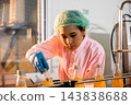 Quality inspector a woman carefully examines beverage bottles on a conveyor 143838688