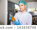 A male worker dressed in a uniform and gloves inspects Basil seed products on the conveyor belt 143838748