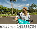 Woman enjoys a ride on her scooter surrounded by greenery 143838764