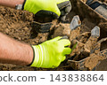 On a sunny day, a worker is adjusting a rotary tiller in preparation for planting crops in the soil. 143838864