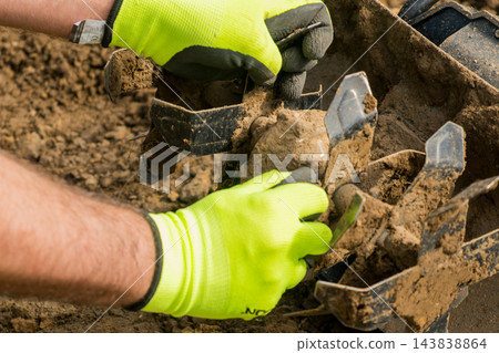 On a sunny day, a worker is adjusting a rotary tiller in preparation for planting crops in the soil. On a sunny day, a worker is adjusting a rotary tiller in preparation for planting crops in the soil. 143838864